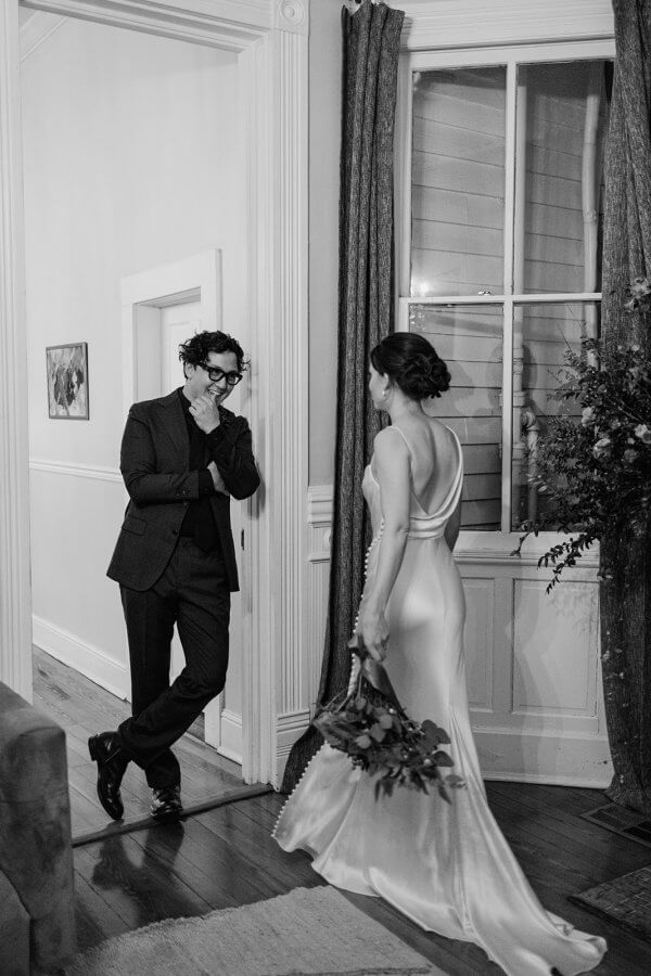 A black and white photo of groom looking at bride holding bouquet of flowers