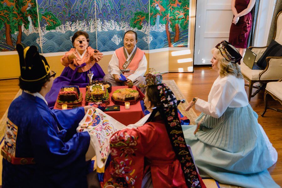 Group in colorful outfits sit for a traditional korean wedding tea ceremony