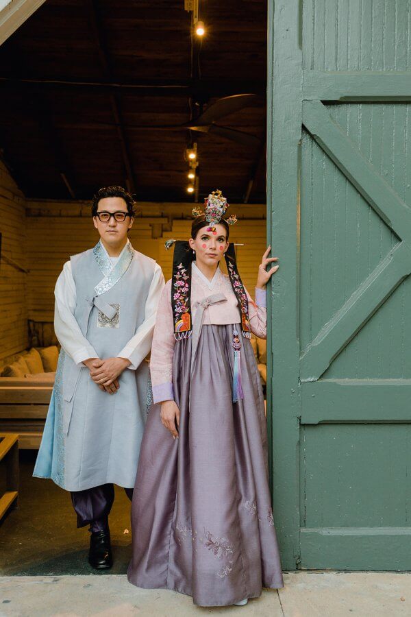 Groom and bride stand in a doorway in traditional Korean hanbok outfits