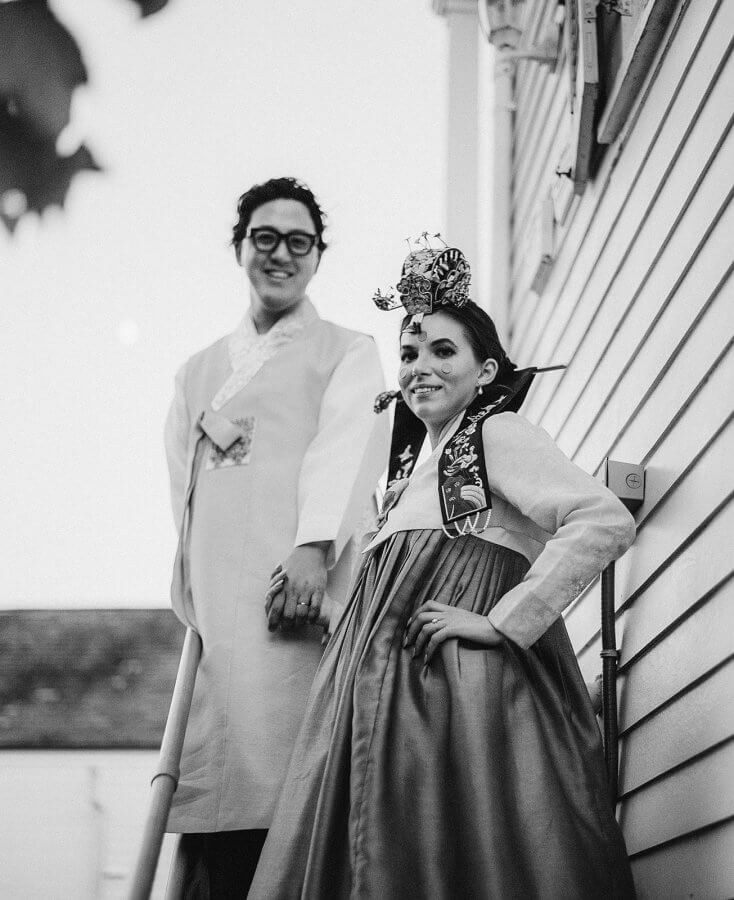 Bride and groom in traditional Korean wedding outfits pose outside on stairs in black and white photo