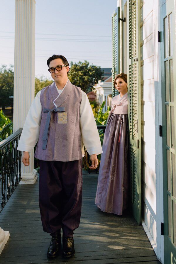 Groom and bride stand on a porch in traditional Korean hanbok outfits
