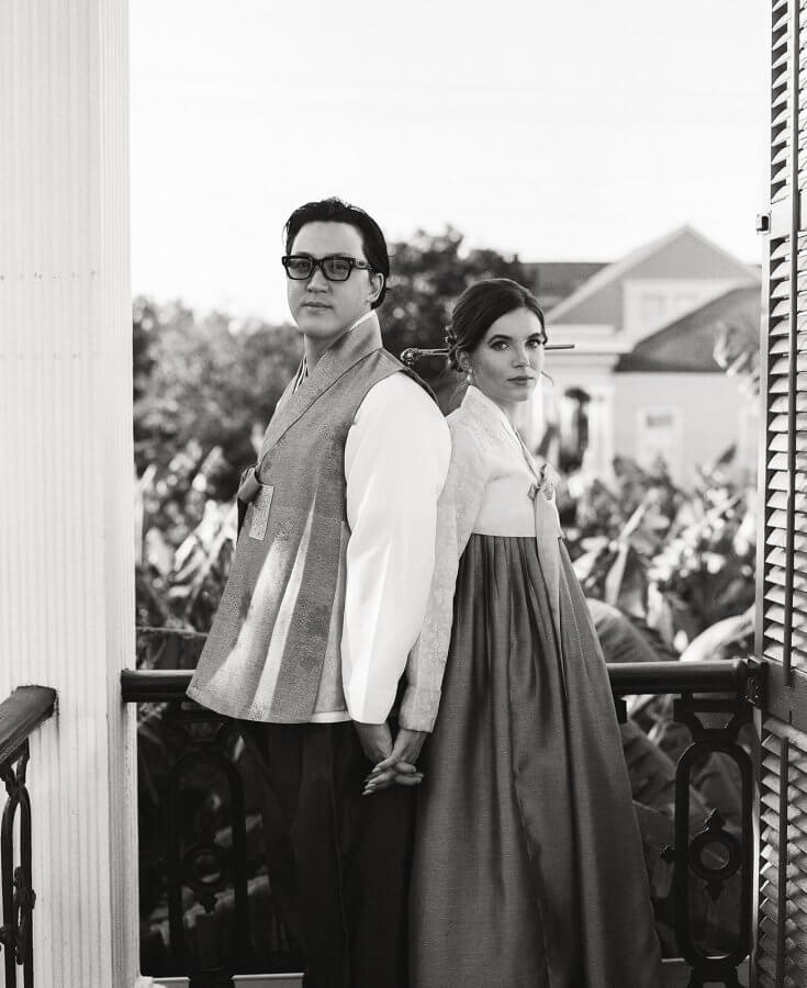 Bride and groom in traditional Korean wedding outfits pose outside on stairs in black and white photo