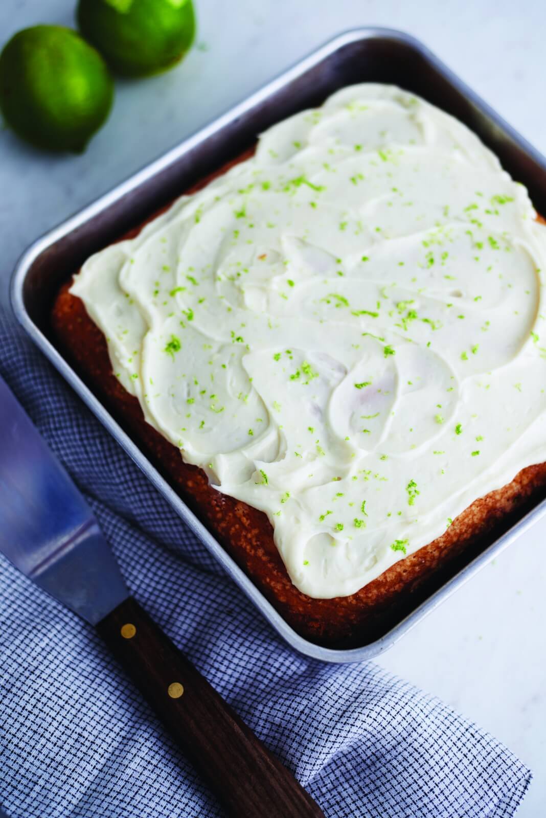 Small lime cake in a square tin with white icing.