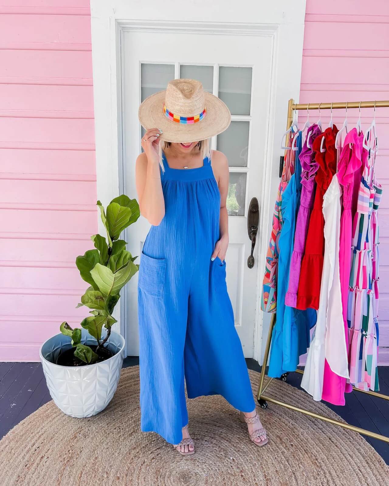 Woman in blue jumpsuit and hat in front of pink background.